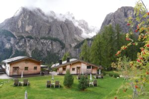 Wooden chalets and lounge chairs below cloud-capped peaks at Kolfuschgerhof Mountain Resort & Spa in the Dolomites