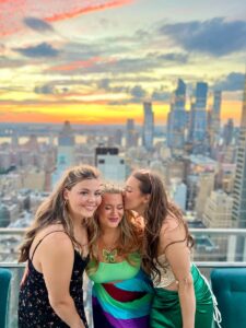 Three women posing on the Nubeluz rooftop above the New York City skyline at sunset