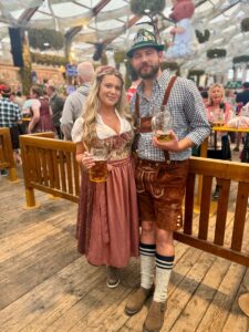 Woman in a dirndl and man in lederhosen holding beer steins inside an Oktoberfest tent in Germany
